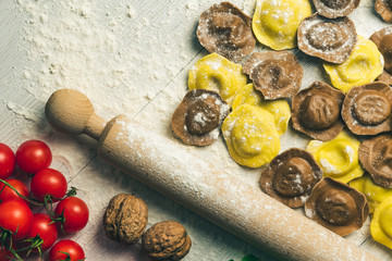 Homemade fresh Italian ravioli pasta on white wood table  with flour,tomatoes,background.
