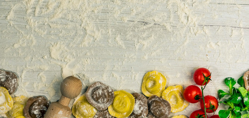 Homemade fresh Italian ravioli pasta on white wood table  with flour, basil, tomatoes,background,top view.