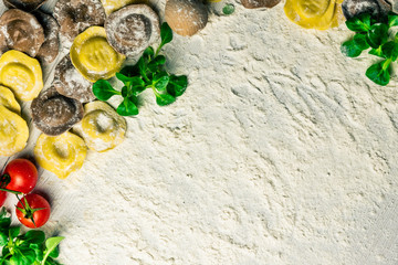 Homemade fresh Italian ravioli pasta on white wood table  with flour, basil, tomatoes,background,top view.