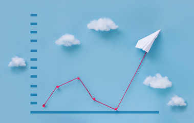 Conceptual paper plane pulling business finance growth chart line upwards on blue sky background. 