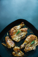Roast chicken in a grill pan decorated with rosemary and meat seasonings on a dark background. View from above.