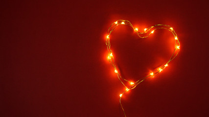 Burning electric garland. The shape of a heart. Glowing lights. Red background. Valentine's day. Feelings and emotions. Love.