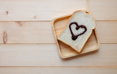 Top view and close up: slice of bread with love sign in heart shape on wooden background. Breakfast concept.	