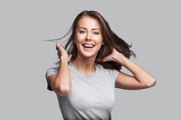 Pretty girl with long hair laughing and enjoying life. Beautiful joyful girl with long brown hair portrait. Isolated on gray background