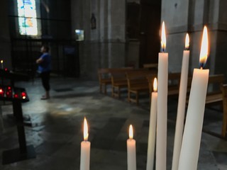Close-up of lighting candles in pedestal of church with woman praying behind