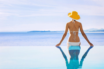 Young woman enjoying a sun in the luxury infinity pool. Enjoying life. Vacations, holidays and summer fun concept