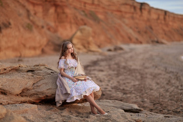 Portrait of a girl near the sea sitting on the rocks with a toy ship in hands.