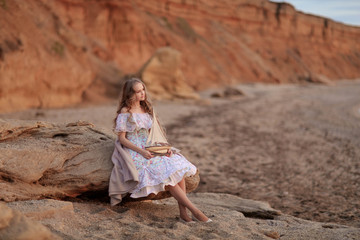 Portrait of a girl near the sea sitting on the rocks with a toy ship in hands.