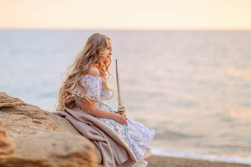 Portrait of a girl near the sea sitting on the rocks with a toy ship in hands.