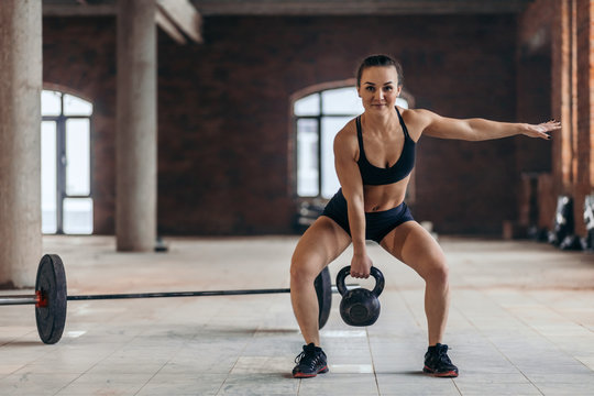 happy fit sweaty woman exercising with kettlebell, doing cross fit workout indoors. copy space. full length photo, hobby, lifestyle, interest, spare time