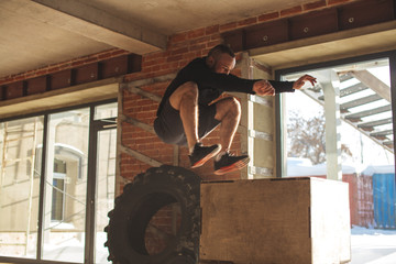 Young male Athlete doing plyo jumps exercise training endurance in crossfit gym. Jumping on the box. Phase touchdown.