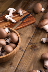 Champignon mushrooms, sacking mat and spices on wooden background. Wooden dishes. Photo in a rustic style. Place for text.