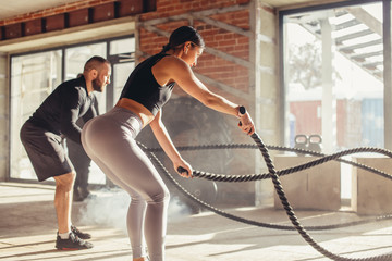 Caucasian fit couple exercising with battle ropes at gym. Woman and man dressed in sports outfit...