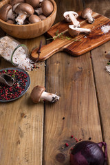 Champignon mushrooms with red onions and spices on a wooden background, wooden utensils. Rustic style photo. Vegetarian lunch of vegetables. Place for text.