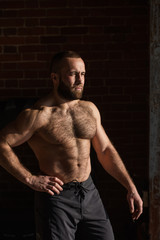 Fototapeta premium Portrait of strong healthy bearded athletic man with naked torso posing against dark wall looking aside
