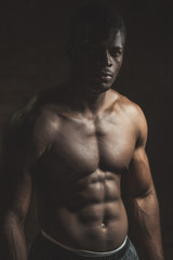 Fototapeta na wymiar Attractive African male fighter or boxer posing shirtless, looking at camera, isolated over dark background.