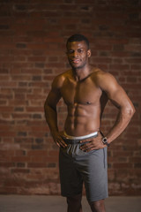 Fototapeta premium Strong afroamerican athletic man with naked perfect shape musculs looking at camera isolated over brick background.