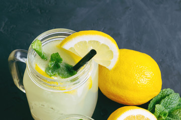 Refreshing lemonade drink with lemon slice and mint in the jar on dark background