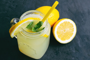 Refreshing lemonade drink with lemon slice and mint in the jar on dark background