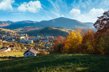 countryside beautiful autumn evening in mountains. small town in the distant valley. colorful trees on the hill. wonderful sunny weather with beautiful sky