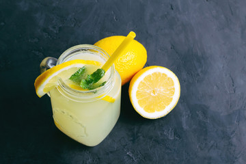 Refreshing lemonade drink with lemon slice and mint in the jar on dark background