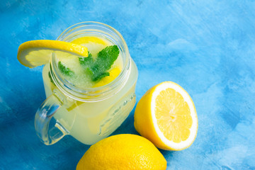 Refreshing lemonade drink with lemon slice and mint in the jar on a blue background