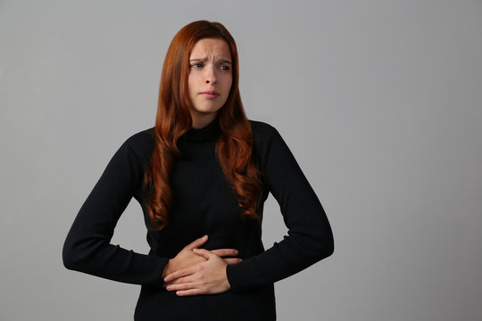The redhead girl has awful stomachache at gray background her home