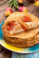A lot of pancakes with red caviar, on a wooden table. A bouquet of tulips. Food for the traditional spring festival in Russia. Thin Russian pancakes with filling.
