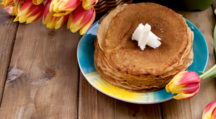 Russian pancakes with butter on a wooden background. A bouquet of fresh spring tulips and traditional Russian food. Free space for text.
