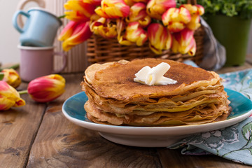 Russian pancakes with butter on a wooden background. A bouquet of fresh spring tulips and traditional Russian food. Free space for text.