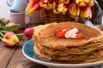 Russian pancakes with butter on a wooden background. A bouquet of fresh spring tulips and traditional Russian food. Free space for text. Banner