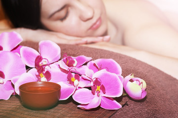 Fototapeta na wymiar Young woman at spa procedure, pink orchid and oil