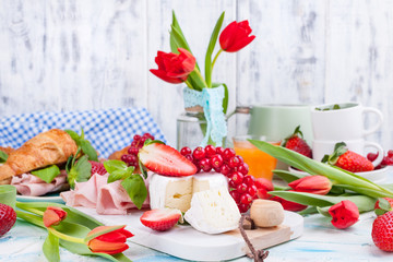 Sweet spring breakfast with croissants and bacon on a light background. A bouquet of red tulips and fresh berries of strawberries and currants. The concept of holiday celebration. brie cheese for 
