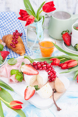 Sweet spring breakfast with croissants and bacon on a light background. A bouquet of red tulips and fresh berries of strawberries and currants. The concept of holiday celebration. brie cheese for 