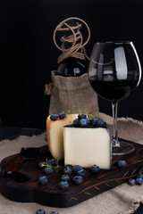 White pecorino cheese and blueberries. Traditional Italian hard cheese and a glass of red wine. Wooden background and dark style photo. Cheese typical of sardinia. Copy space.