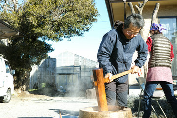 An older man making mochi in his garden with his family around him