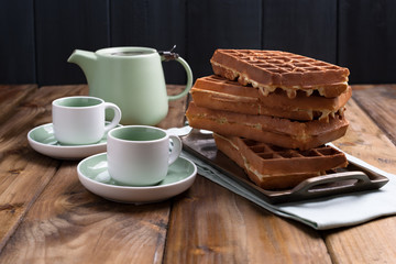 Two mugs of tea and teapot on a wooden table. Fresh homemade waffles. Traditional breakfast. Free space for text.