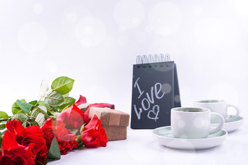 A bouquet of red roses and fresh aromatic tea for a romantic breakfast. Words of love on a note and a gift with flowers. Valentine's day and mother's day concept. Copy space.