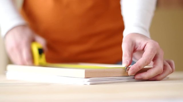 Female carpenter tape measuring picture frame in small business woodwork workshop, close up of hands