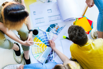 Closeup top view of creative workers having informal meeting in light office space. Architects and interior designers working on floor with color samples, room layouts, supplies. Teamwork concept.