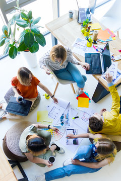 Top View Of Creative Workers Having Informal Meeting In Office Space. Architects And Interior Designers Working On Floor With Color Samples, Room Layouts, Laptops, Supplies. Teamwork Concept.