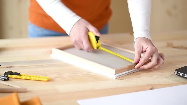 Female carpenter tape measuring picture frame in small business woodwork workshop, close up of hands