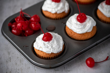 Homemade muffins with cream and cherry on the muffin tin.