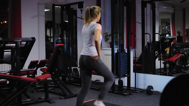 View from the back on a young healthy woman performing cardio training using a step-board in front of the mirror. Sport and health concept.