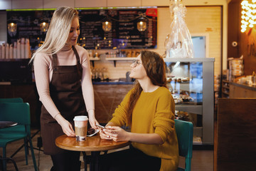 Young pretty woman and waitress in cafe.