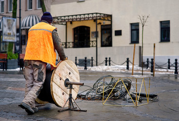 Open sewage manhole with cable on coil spool, provider company working on connection internet using fiber optic stand for wire uncoiling. Cable spool on the axle, worker unwinds wire during repair