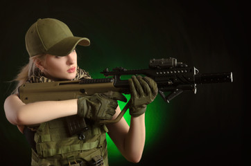 the girl in military special clothes posing with a gun in his hands on a dark background in the haze