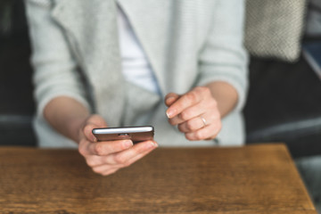 Woman holding her cellular in hands and sitting behind wooden table