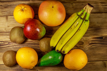 Assortment of tropical fruits on wooden table. Still life with bananas, mango, oranges, avocado, grapefruit and kiwi fruits