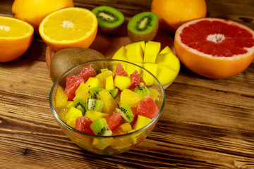 Fototapeta na wymiar Tasty fruit salad in glass bowl and fresh fruits on the wooden table